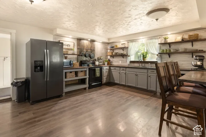 Kitchen featuring wood-finish flooring, grey cabinetry, a stainless steel refrigerator, a black range, and open shelving