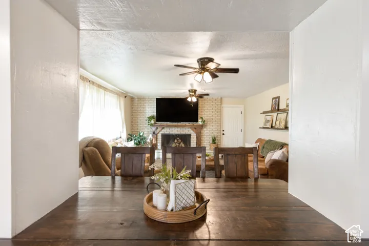 Exposed brick fireplace with a rustic wood mantel, two ceiling fans with integrated lighting, and multiple wall-mounted display shelves
