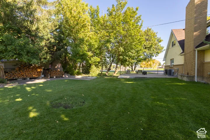 Expansive lawn area with a concrete patio, mature trees, and a brick chimney exterior
