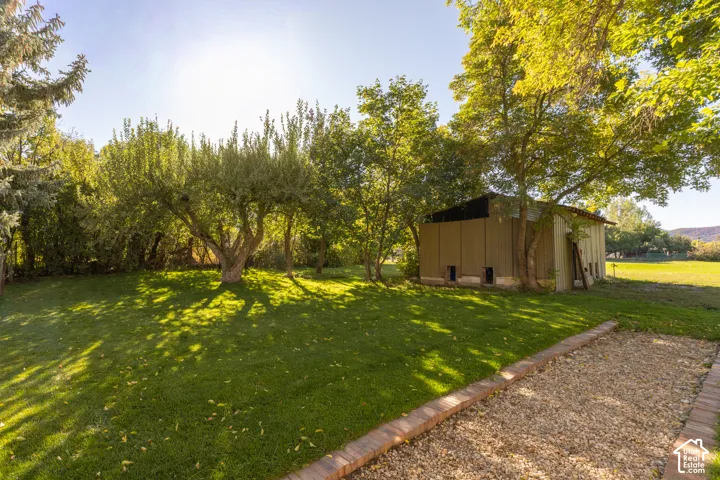 Expansive lawn area with mature trees, a gravel pathway with brick edging, and a detached outbuilding