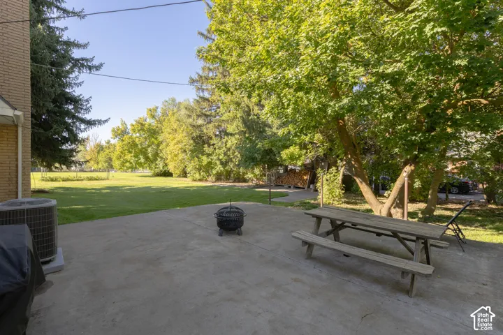 Expansive concrete patio with a large grassy area, mature trees, and a brick exterior