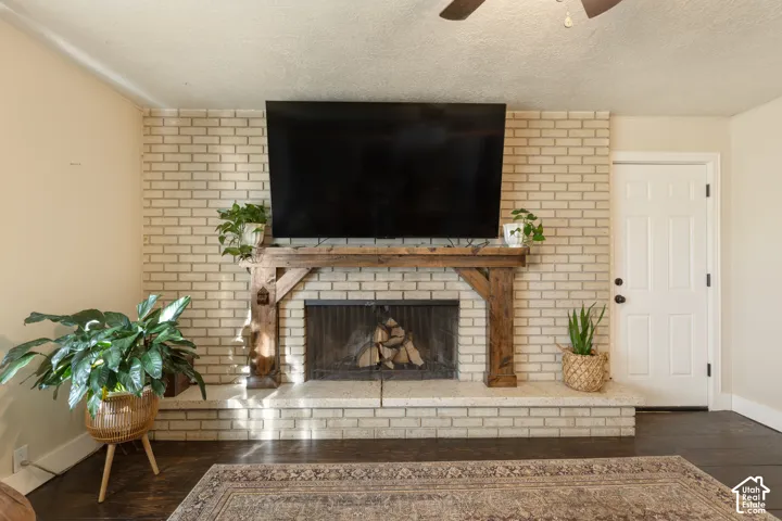 Brick fireplace with a wood-beam mantel, dark wood-finish flooring, and a paneled white door