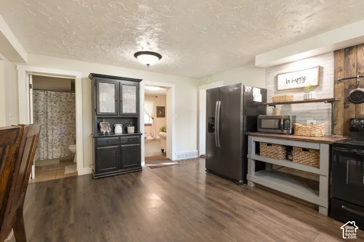 Hardwood-look flooring, built-in black hutch, modern black refrigerator, wood-finish countertop, and decorative wall paneling