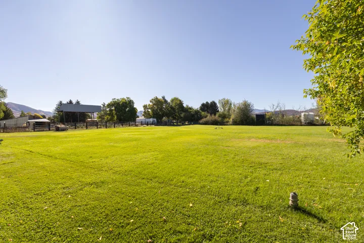 Expansive grassy lawn with a partial wood-post fence and distant outbuildings