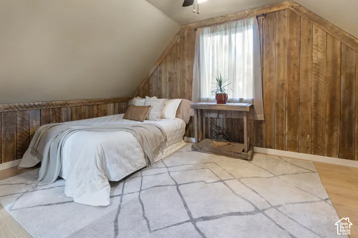Sloped ceiling with recessed lighting, wood-finish accent wall, built-in window and window treatment, and light wood-finish flooring