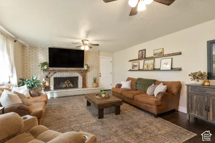 White-painted brick fireplace with a wood mantle, ceiling fan with integrated lighting, wood-finish flooring, and built-in wall shelving