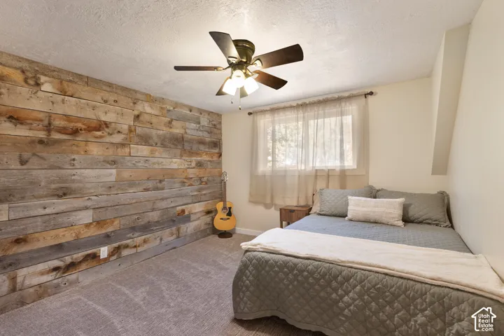 Wood accent wall, ceiling fan with integrated lighting, window with curtain rod, textured ceiling finish, carpeted flooring
