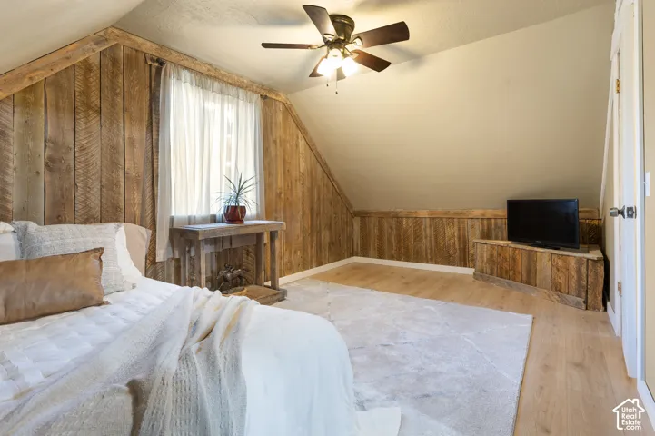 Wood-finish plank flooring, wood-paneled walls, and a ceiling fan with integrated lighting