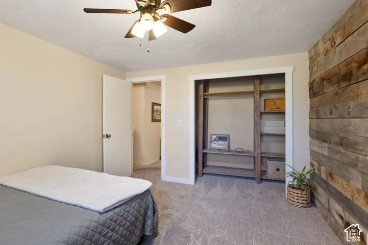 Wall-mounted wood paneling with natural finish, ceiling fan with integrated lighting, built-in closet shelving, and light-toned carpeting