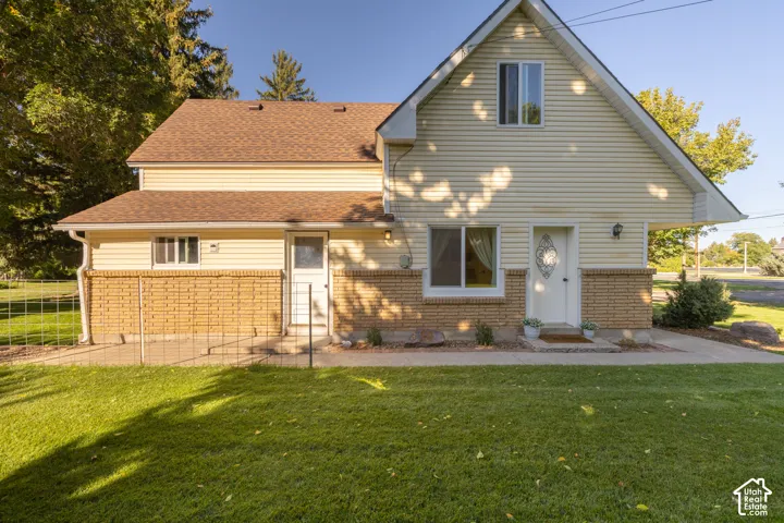 Exterior featuring light-colored siding, brick detailing, a brown shingle roof, and a green lawn