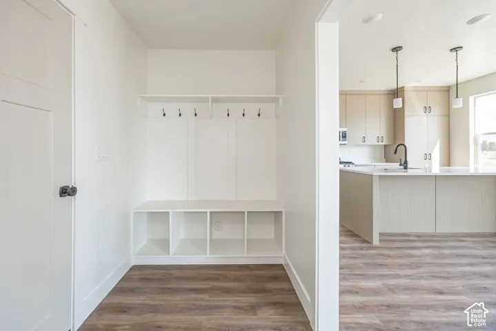 Built-in mudroom bench with cubby storage and coat hooks, wood-finish flooring, and a contemporary kitchen with light-toned cabinetry, a spacious island, and pendant lighting