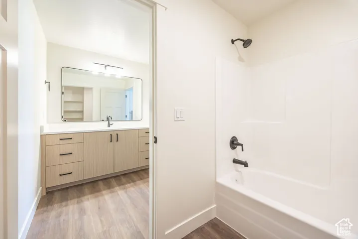 Bathroom featuring a white bathtub with dark fixtures, light wood-finish flooring, a vanity with light wood-finish cabinetry, a white countertop, and a large rectangular mirror