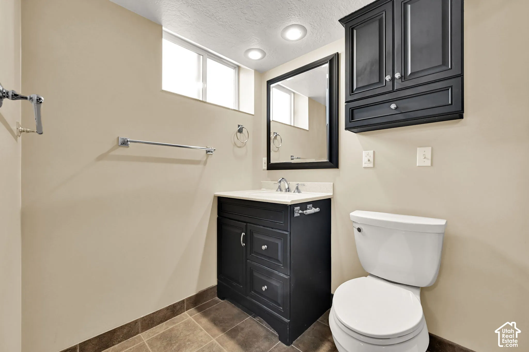 Bathroom featuring a dark wood vanity with a light-toned countertop, a matching dark wood wall cabinet, an integrated toilet, and tiled flooring