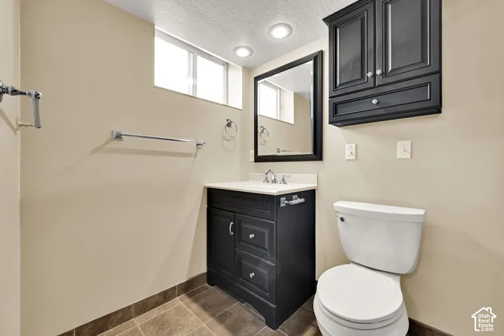 Bathroom featuring a dark wood vanity with a light-toned countertop, a matching dark wood wall cabinet, an integrated toilet, and tiled flooring