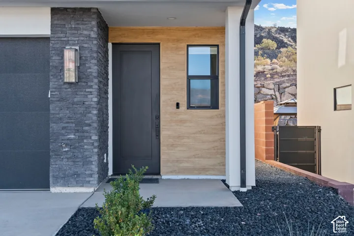 Modern exterior featuring dark stacked stone, a contemporary black entry door, an exterior wall light fixture, a black framed window, and black rock landscaping