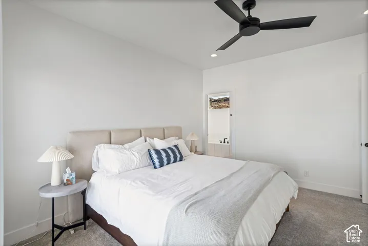 Recessed ceiling lighting, ceiling fan, carpet flooring, and a door leading to a bathroom featuring a built-in tub