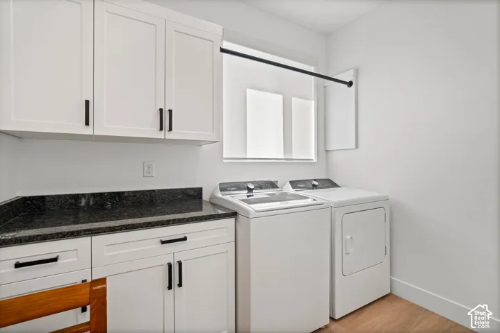 Laundry area featuring white cabinetry with black hardware, dark countertop, and wood-finish flooring