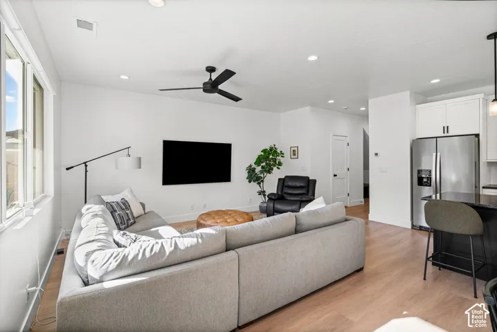 Open concept living space featuring wood-finish flooring, recessed lighting, a modern ceiling fan, stainless steel refrigerator, and white upper cabinetry