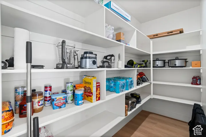 Spacious pantry featuring extensive built-in shelving with white finish, ample storage capacity for dry goods and small appliances, wood-finish flooring, and recessed lighting throughout