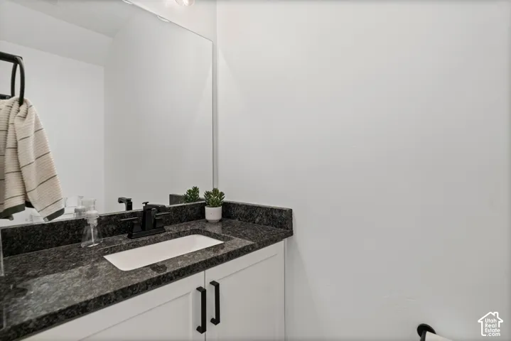 White vanity with a rectangular undermount sink, dark stone countertop, and matte black faucet