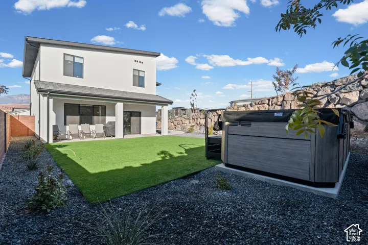 Modern two-story exterior with a covered patio, artificial turf lawn, built-in hot tub, and rock landscaping