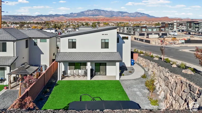 Modern exterior with a white stucco finish and dark trim, featuring a covered patio, a green turf lawn, and a stone retaining wall