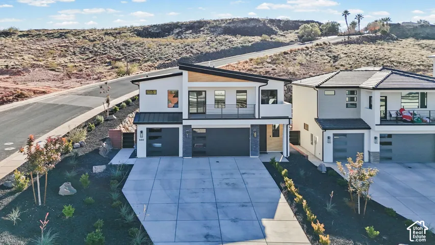 Modern architectural design with a flat roofline, two-car garage, and an upper-level balcony with metal railing