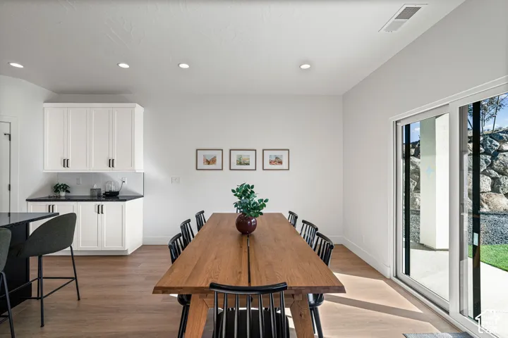 Wood-finish flooring throughout the dining area, white upper and lower cabinetry with black hardware, black countertops, and recessed lighting