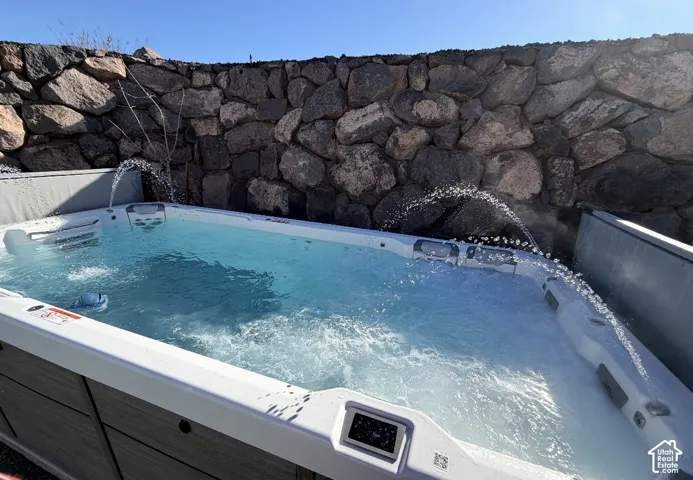 Swim spa with multiple water features, integrated controls, and a surrounding stone retaining wall