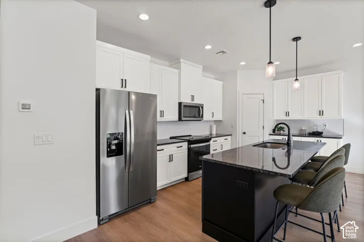 Modern kitchen featuring white cabinetry, wood-finish flooring, a kitchen island with seating, stainless steel appliances, and pendant lighting
