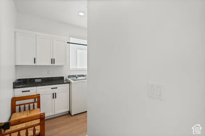 White shaker-style cabinetry with black hardware, dark stone countertop, wood-finish flooring, and recessed lighting