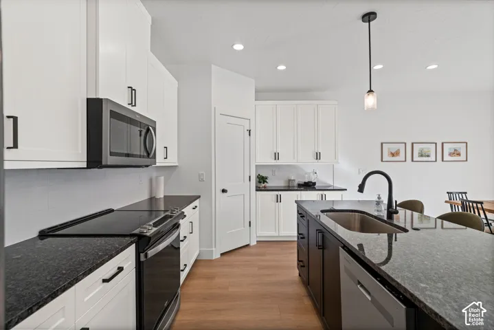 White shaker-style cabinetry with matte black hardware, dark countertops, built-in microwave, and wood-finish flooring