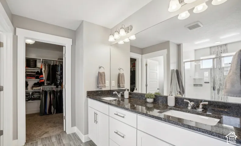 Double vanity with integrated sinks, granite-finish countertop, white cabinetry with brushed nickel hardware, and wood-finish flooring