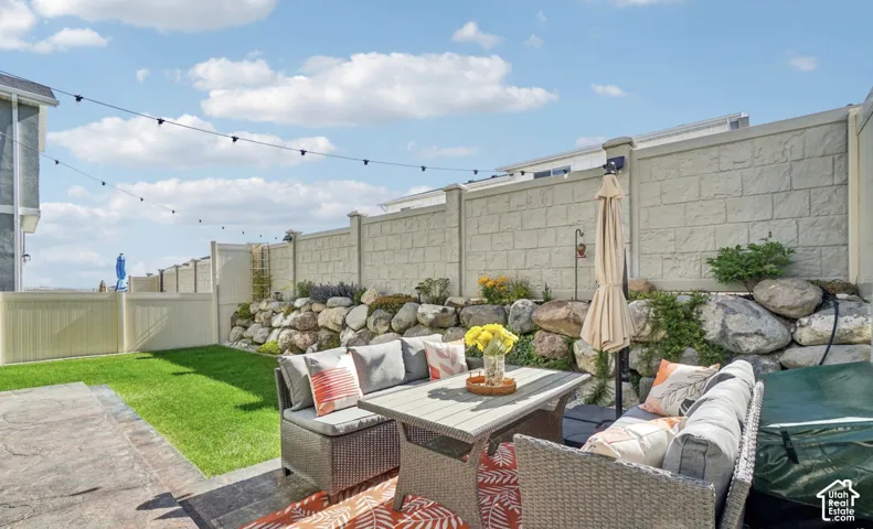 Paved patio area, manicured lawn, stone retaining wall, block privacy fence, and string lighting