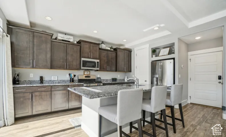 Kitchen featuring wood-finish flooring, recessed lighting, and an island with a built-in sink and granite-style countertop