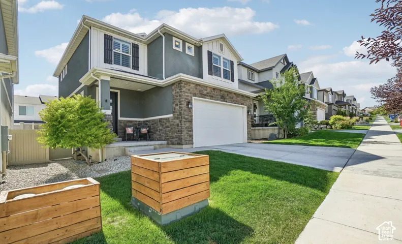 Two-story exterior with stone veneer accents, an attached garage, a covered entry porch, a concrete driveway, and a sidewalk