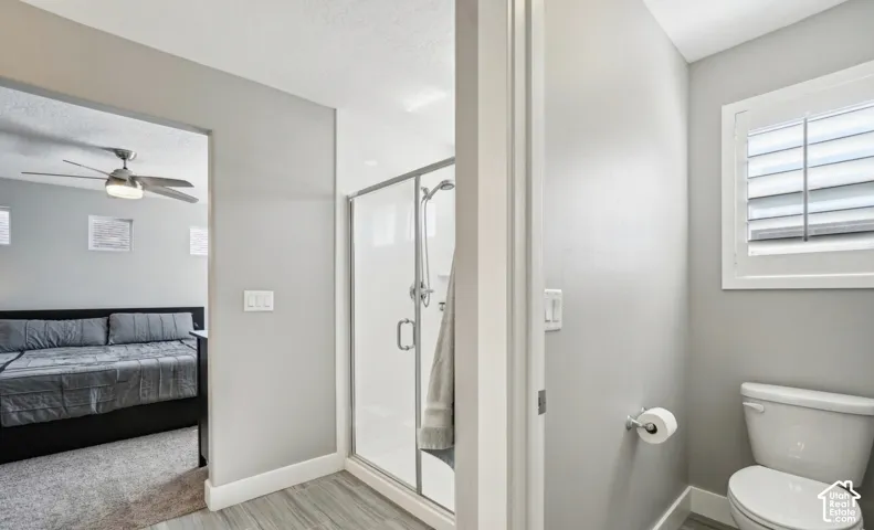 Shower enclosure with glass door, white toilet, and window with plantation shutters