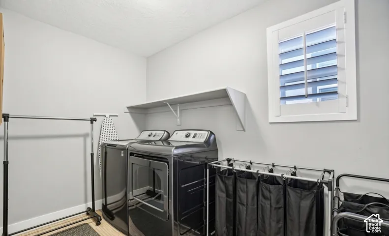 Dedicated laundry area featuring a white wall shelf, a window with white plantation shutters, and light-colored wood-finish flooring