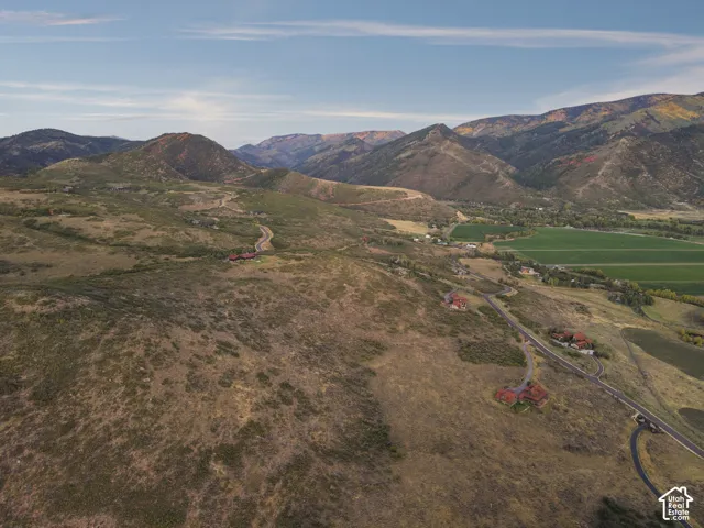 Expansive mountainous terrain featuring scattered residences, winding roads, and distant green fields