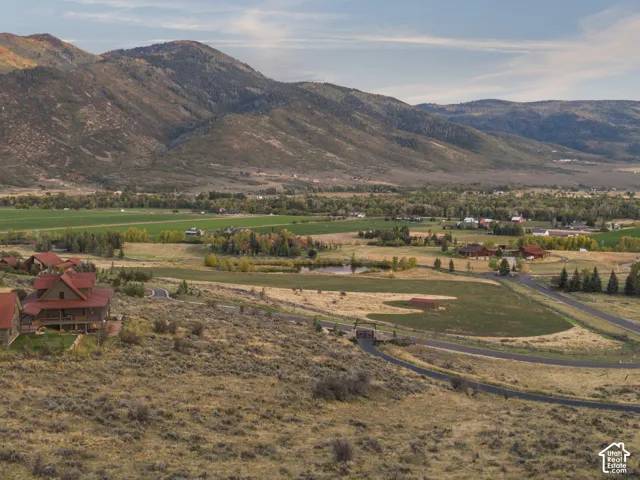 Mountain backdrop, expansive valley, scattered residential properties, paved driveways, natural landscape