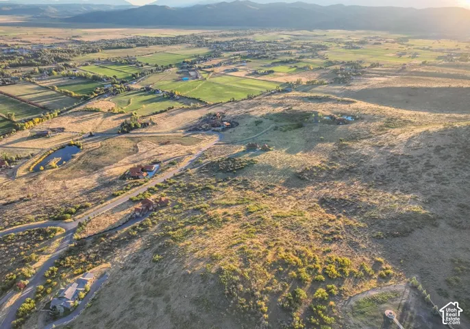Expansive landscape featuring scattered residential properties, a tranquil pond, and distant mountain ranges