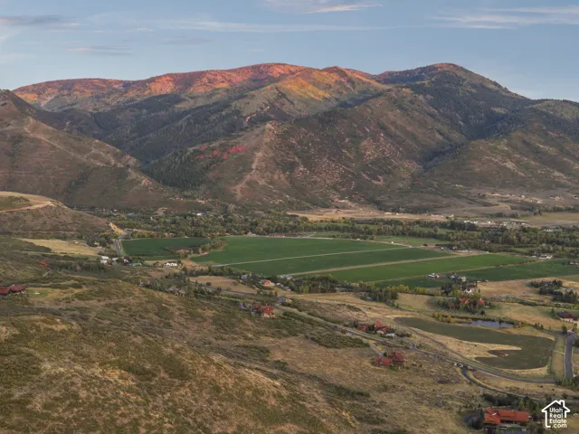Expansive mountain and valley scenery featuring distant residential structures, green fields, and a prominent mountain range