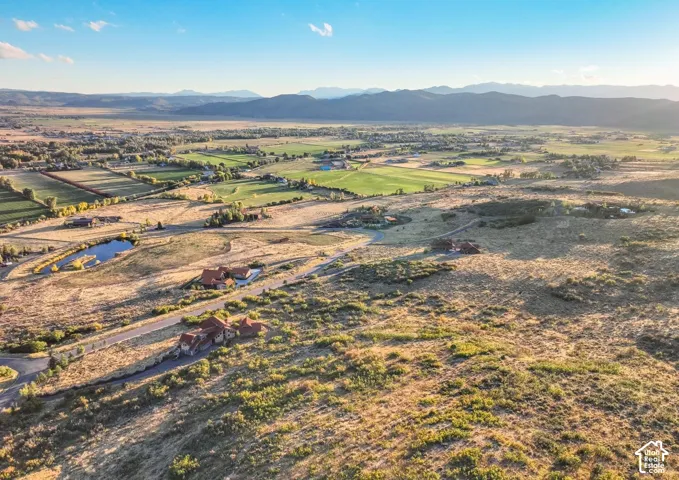 Expansive natural landscape with distant mountain ranges, scattered residential properties, and a visible pond feature