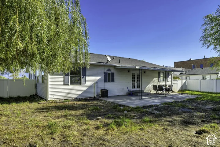 Expansive backyard with a covered concrete patio, white vinyl fencing, and mature trees