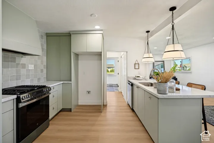 Contemporary kitchen featuring wood-finish flooring, light-toned cabinetry, an integrated range hood, a stainless steel range, and a kitchen island with pendant lighting