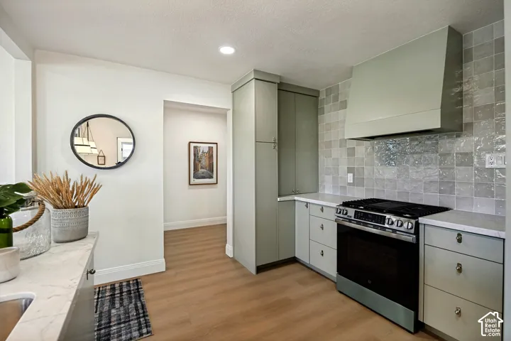 Kitchen featuring wood-finish flooring, light-toned cabinetry, a built-in oven with a gas cooktop, a tile backsplash, and light-toned countertops