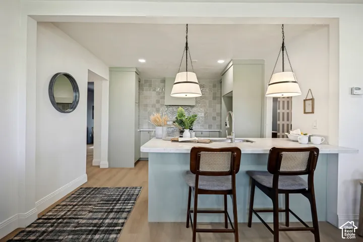 Kitchen featuring an island with seating, pendant lighting, light-toned cabinetry, a patterned tile backsplash, and wood-finish flooring