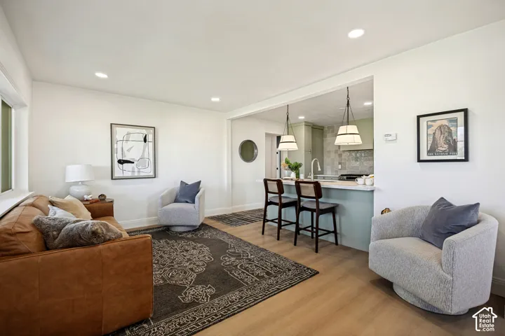 Recessed ceiling lighting, wood-finish flooring, white walls, and a kitchen pass-through with pendant lighting