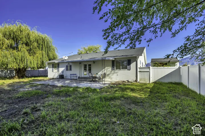 Expansive rear yard featuring a concrete patio, vinyl fencing, and mature trees