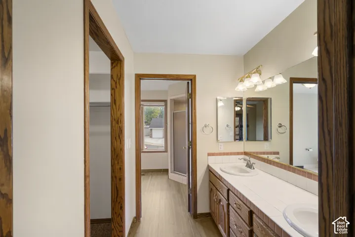 primary bathroom with Dual sink vanity with wood-finish cabinetry, tile countertop, and a large mirror